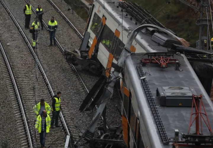 Bomberos y trabajadores de emergencia están parados junto a los vagones descarrilados del tren cerca de Barcelona. EFE