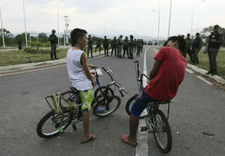 Dos niños en bicicleta frente a soldados venezolanos que bloquean el paso por el puente internacional de Tienditas. Foto: AP