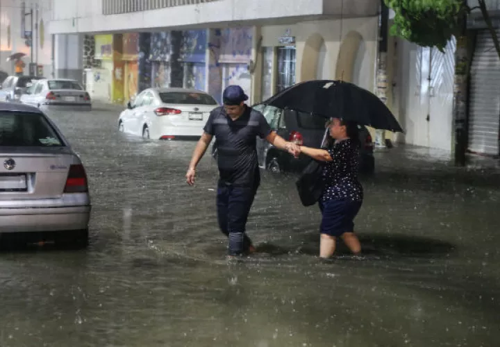  Dos personas cruzan una calle inundada en el puerto de Acapulco por el huracán Rosa. 
