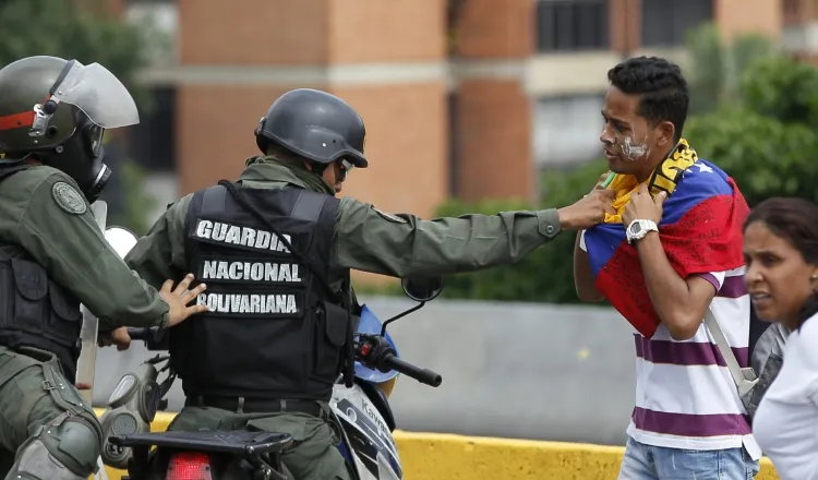 Un policía detiene a un joven. /Foto AP