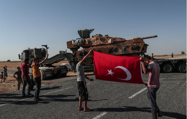 Jóvenes con la bandera turca al paso de blindados militares turcos en el noreste de Siria. Foto: EFE.