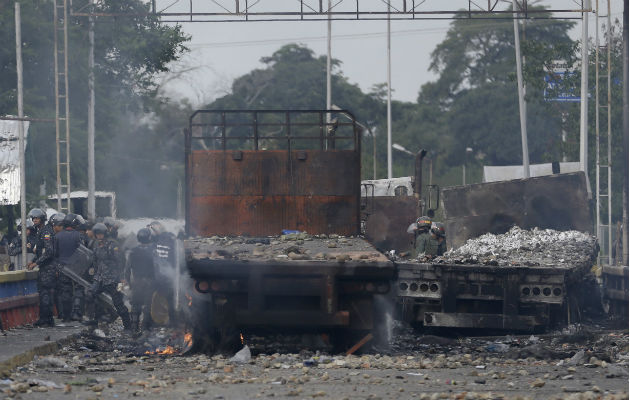 Guardias chavistas junto a dos camiones quemados. Foto: EFE.